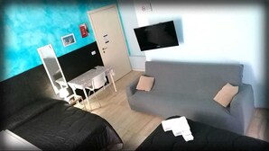 A room with a bed, a sofa, a small table with a chair, a TV mounted on the wall, and a door. - A Due Passi B&B (Catania)