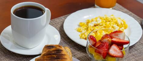 Un desayuno con una taza de café, huevos revueltos, un croissant y un vaso de jugo de naranja sobre una mesa.