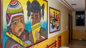 Un pasillo con un gran mural de dos figuras tocando un instrumento tradicional, un banco y otro mural más pequeño en la pared.