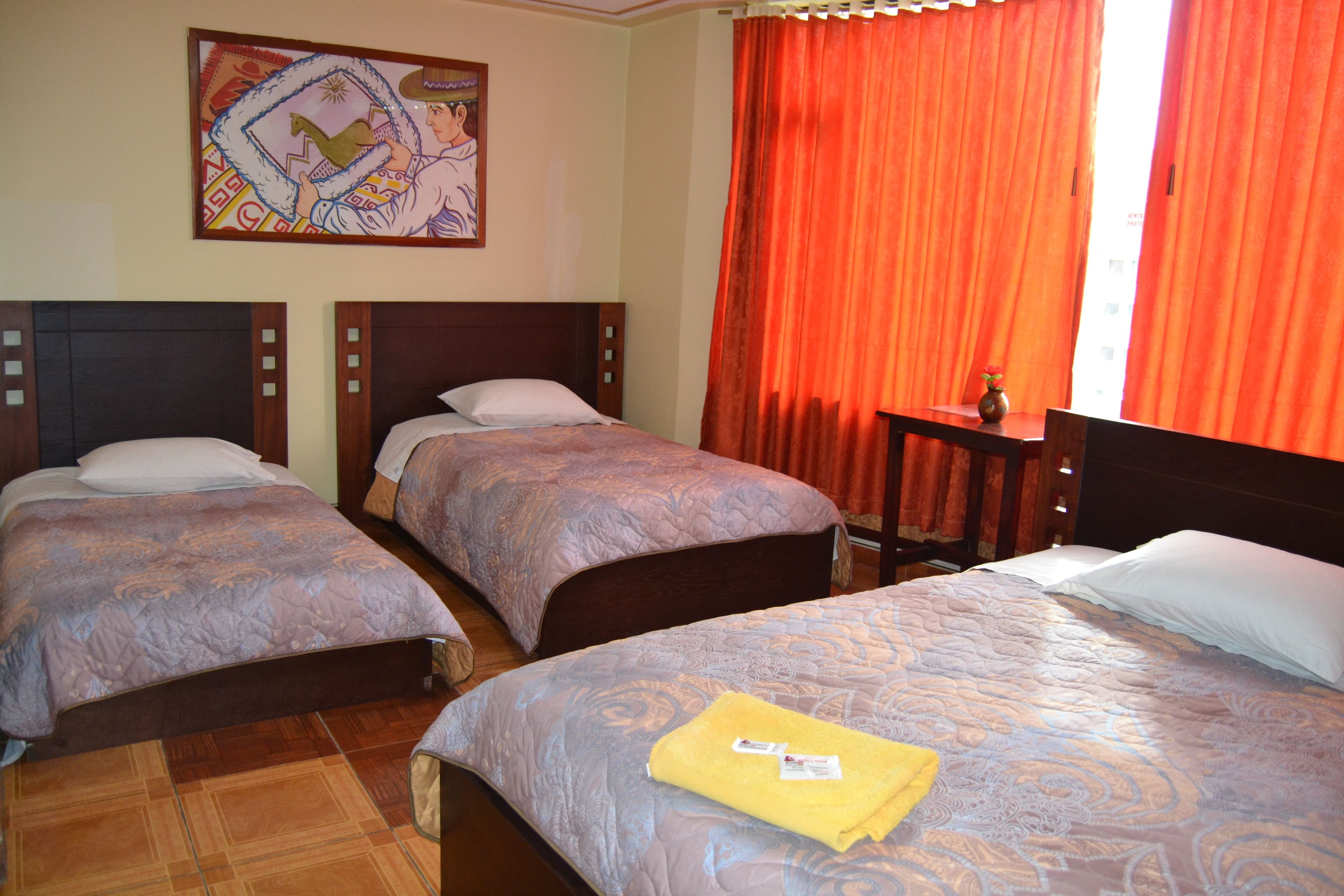 A hotel room with two single beds, a large bed, and a small table with a vase.