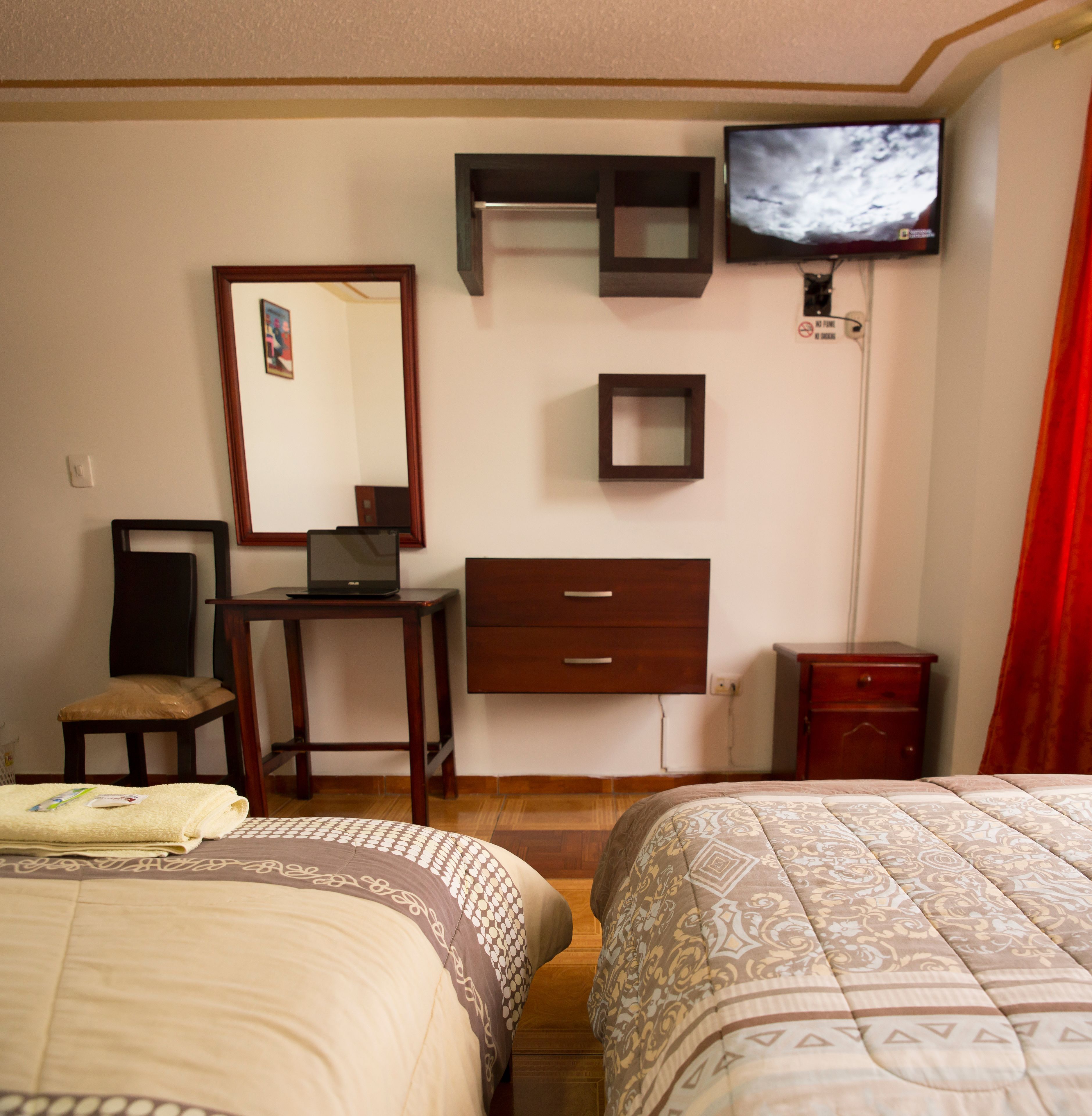 Habitación de hotel con dos camas, un escritorio con una computadora portátil, un televisor en la pared y un espejo.