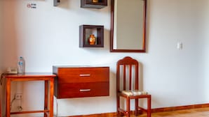 Una habitación de hotel con un aparador de madera, una silla, una mesita con una botella, un espejo y un televisor montado en la pared.