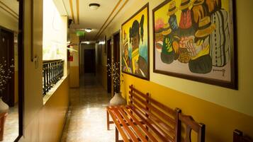 A hallway with a wooden bench, yellow walls, and two framed paintings.