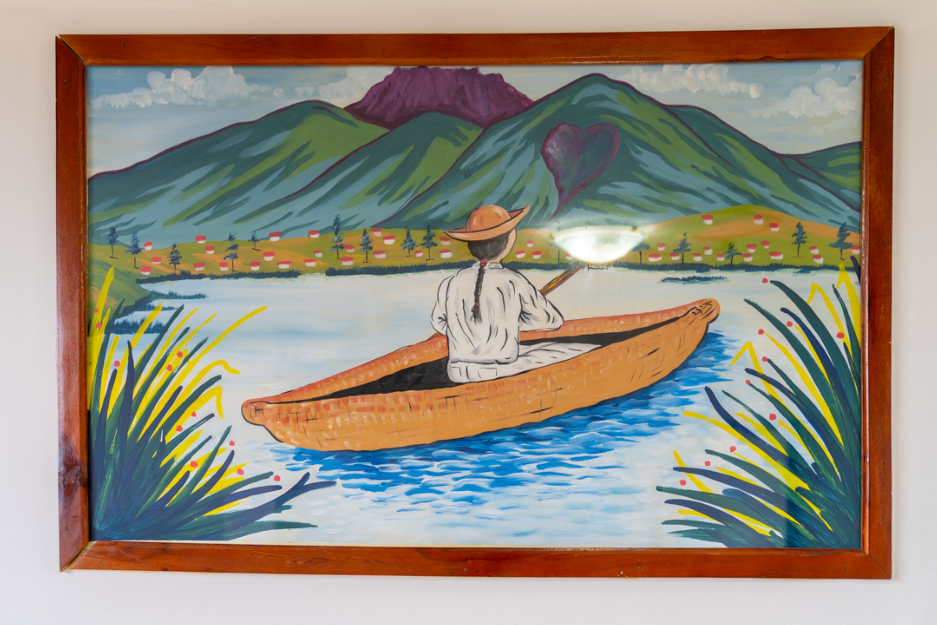 Pintura emoldurada de uma pessoa em um barco a remo em um rio, com montanhas ao fundo.