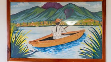 Pintura emoldurada de uma pessoa em um barco a remo em um rio, com montanhas ao fundo.