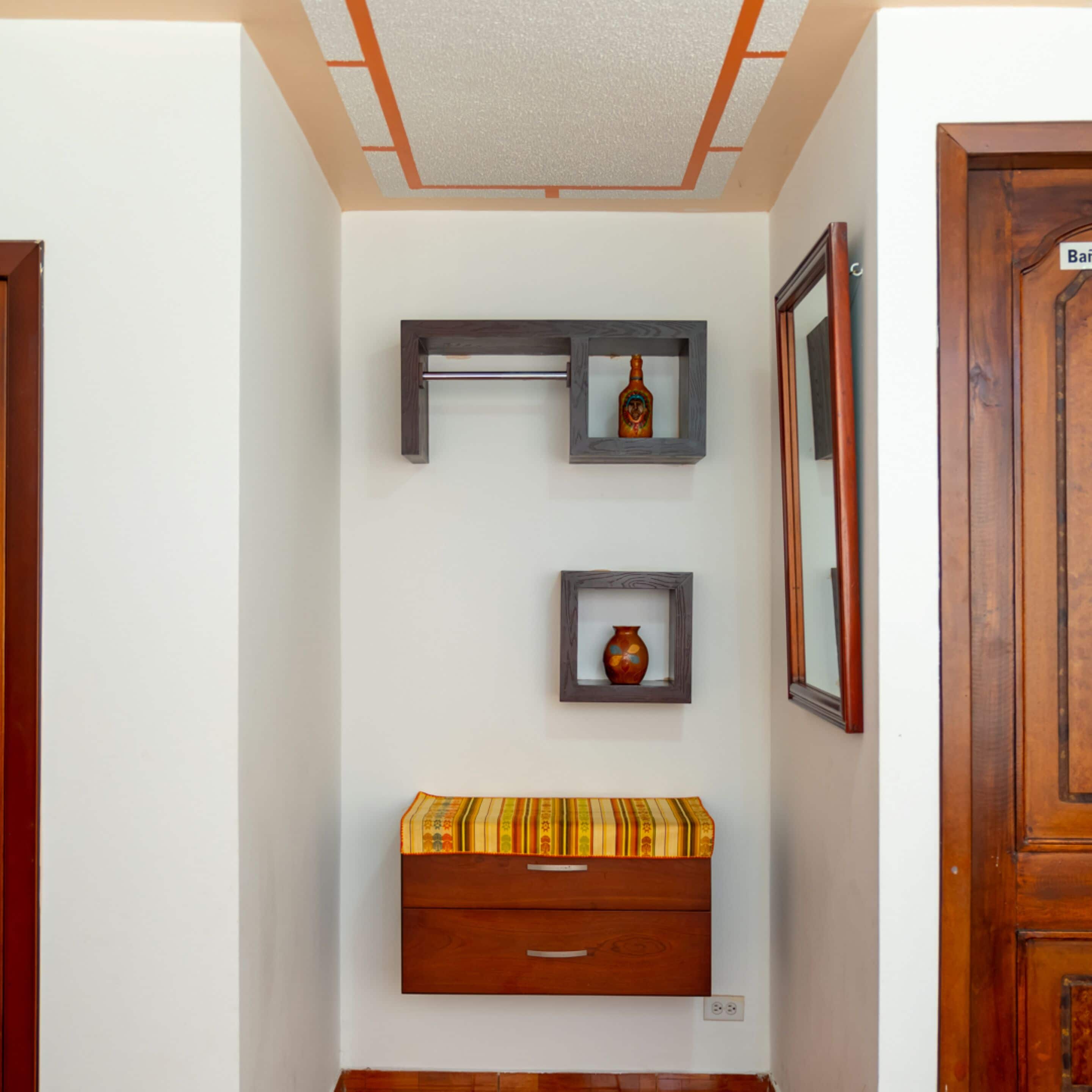 A hallway with a wooden bench, a small shelf with a bottle, and a framed picture on the wall.