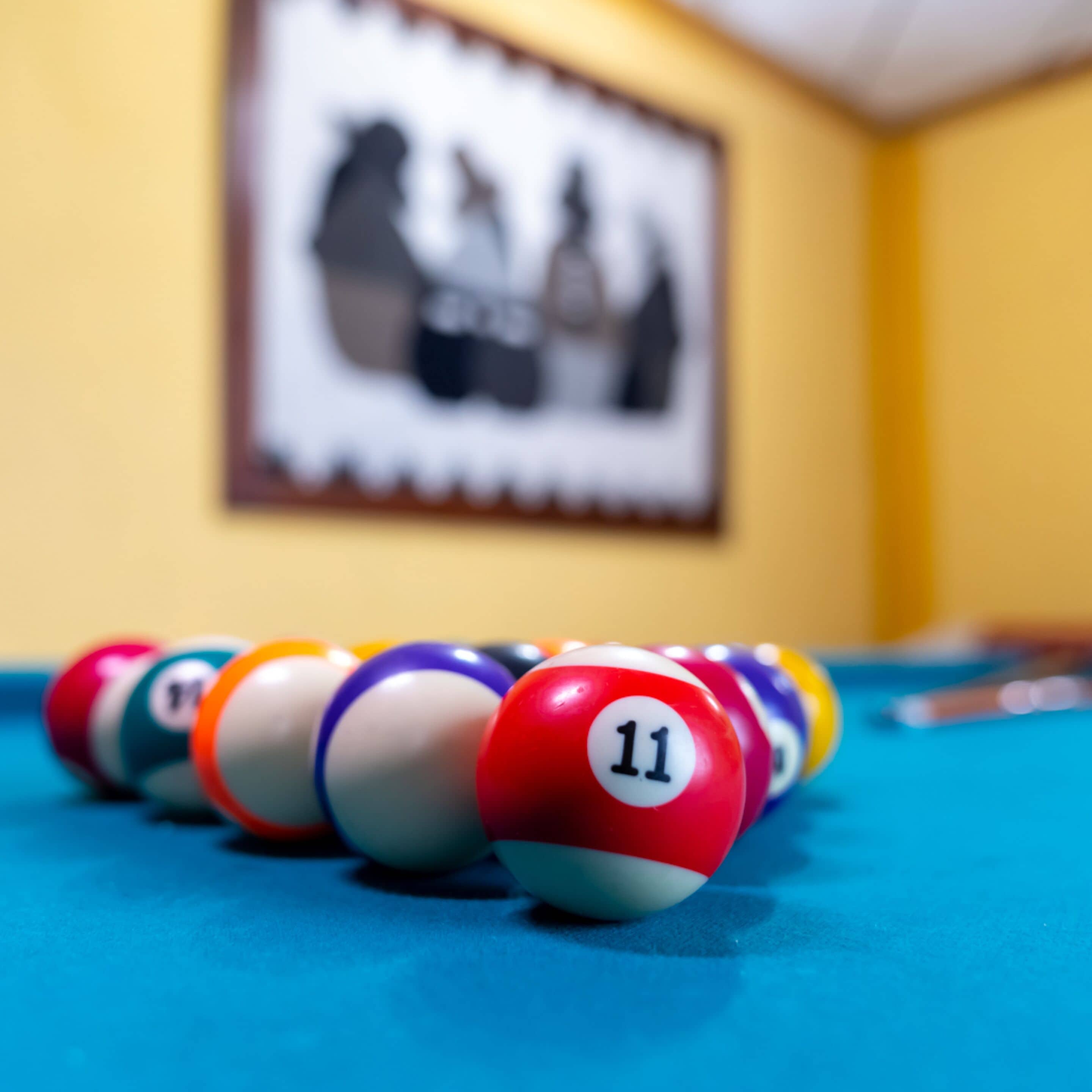 Uma mesa de bilhar com bolas numeradas e um quadro pendurado na parede.