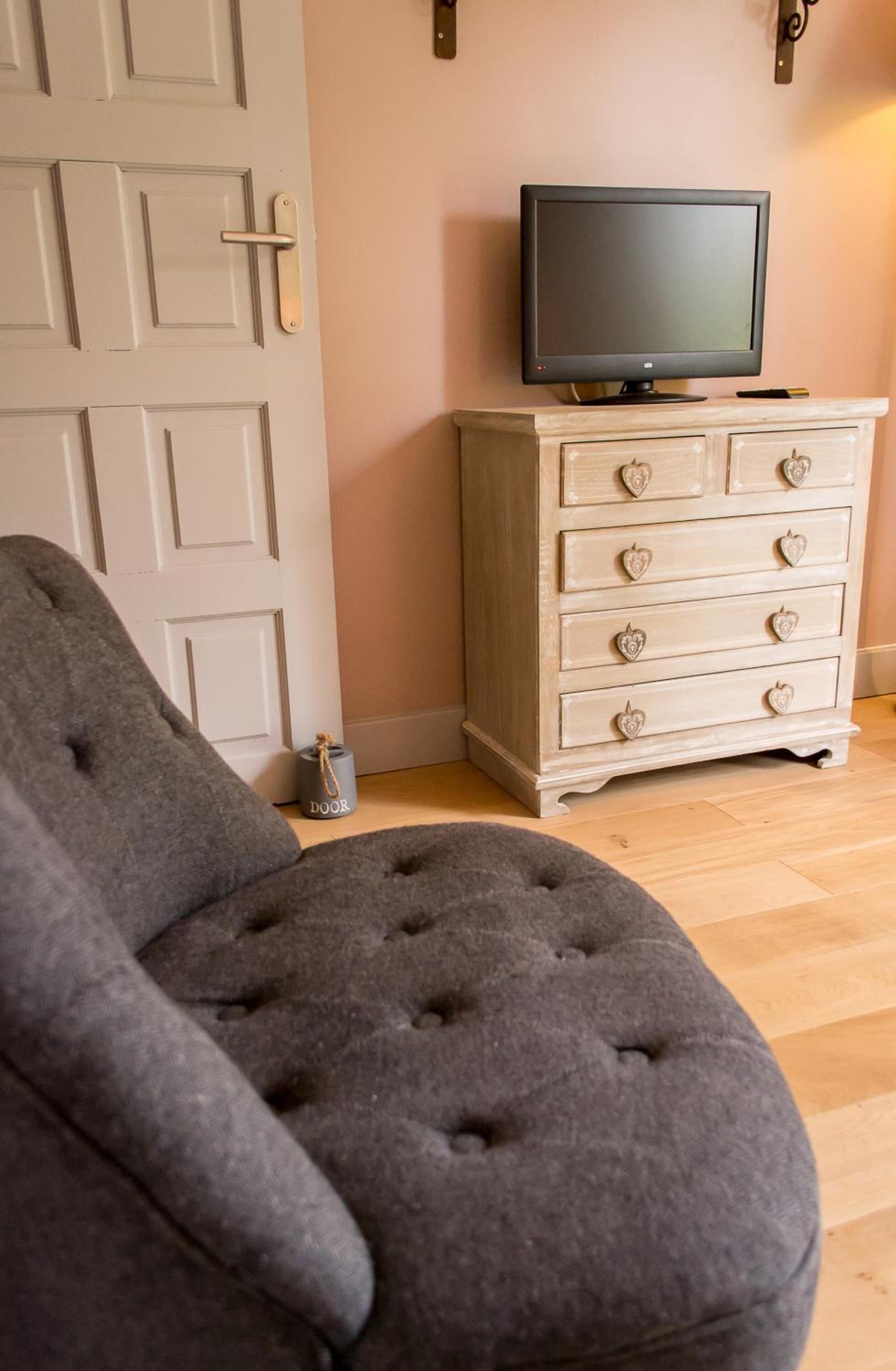 A room with a grey tufted chair, a white dresser with heart-shaped handles, and a television on top.