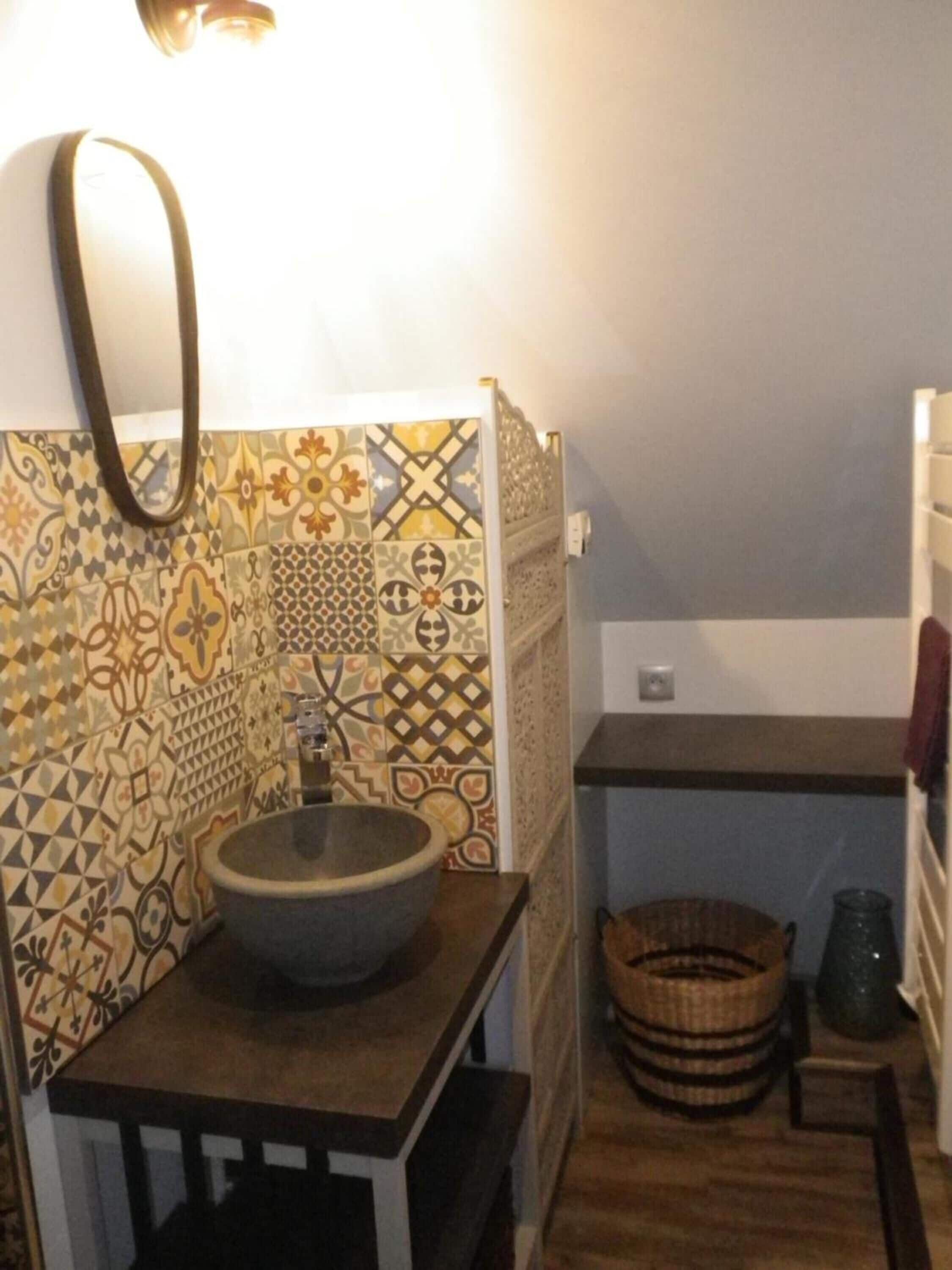 Um banheiro com revestimento de azulejos estampados, uma pia, um porta-toalhas e uma cesta.