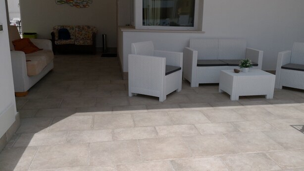 A patio area with white wicker furniture, including two chairs and a small table, and a sofa in the background. - B&B La Maison (Gallipoli)