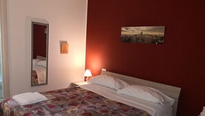 A hotel room with a bed, a nightstand, a lamp, a mirror, and a painting on the wall. - B&B La Maison (Gallipoli)
