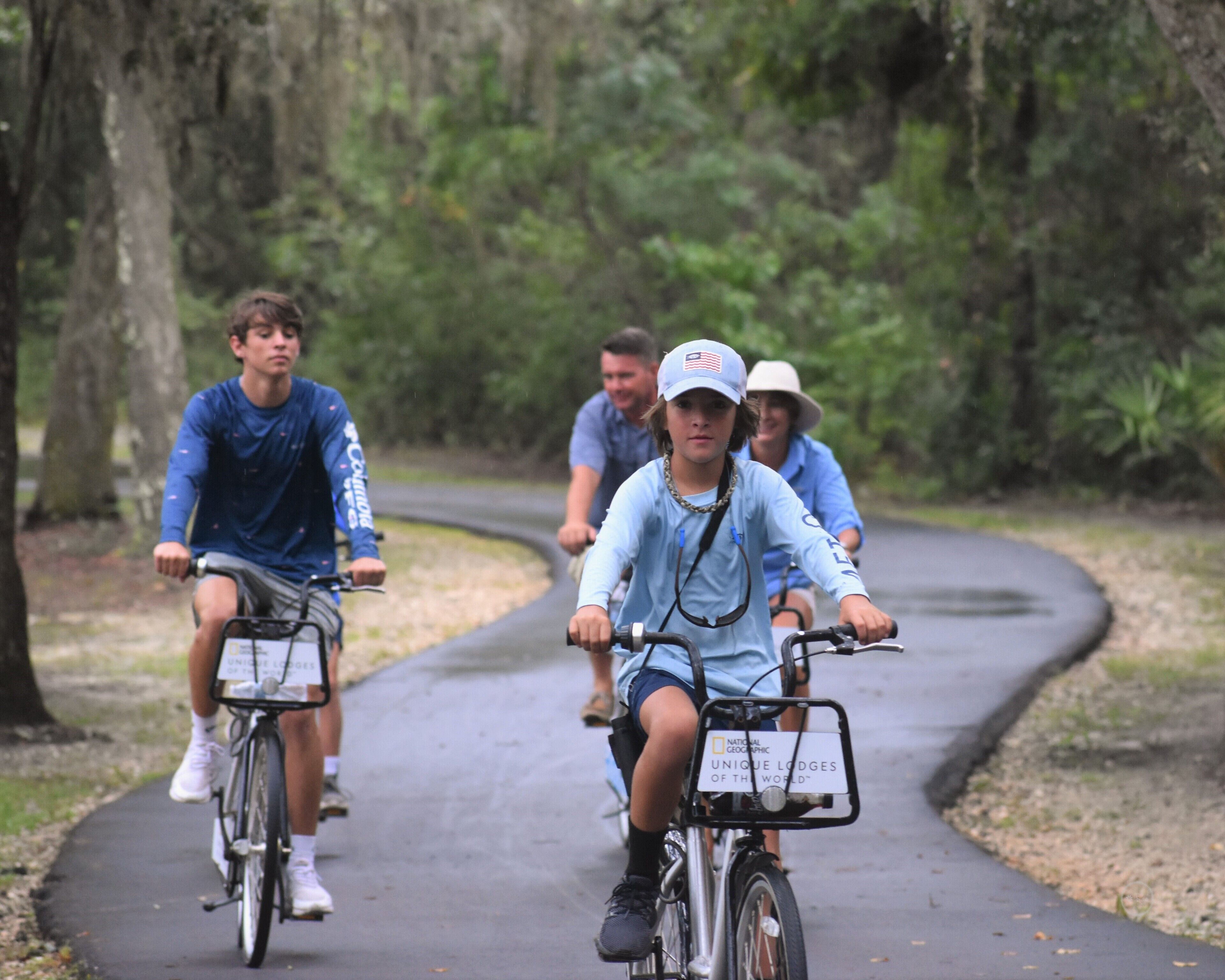 A group of people riding bicycles on a paved path surrounded by trees.