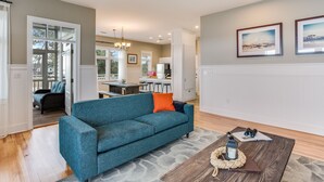 Een woonkamer met een blauwgroene bank, een salontafel en uitzicht op de keuken.