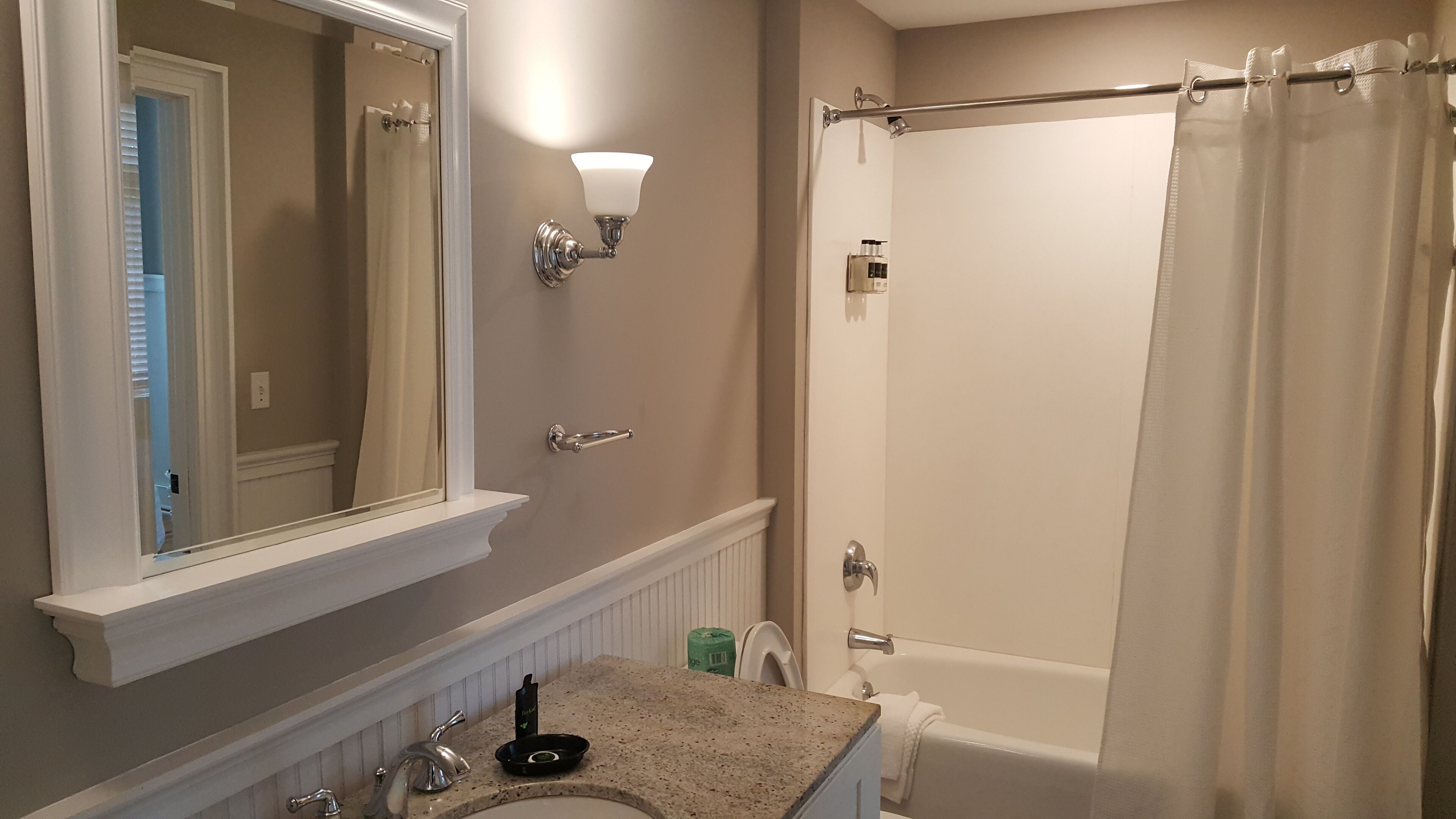 A bathroom with a sink, mirror, light fixture, and a shower curtain.