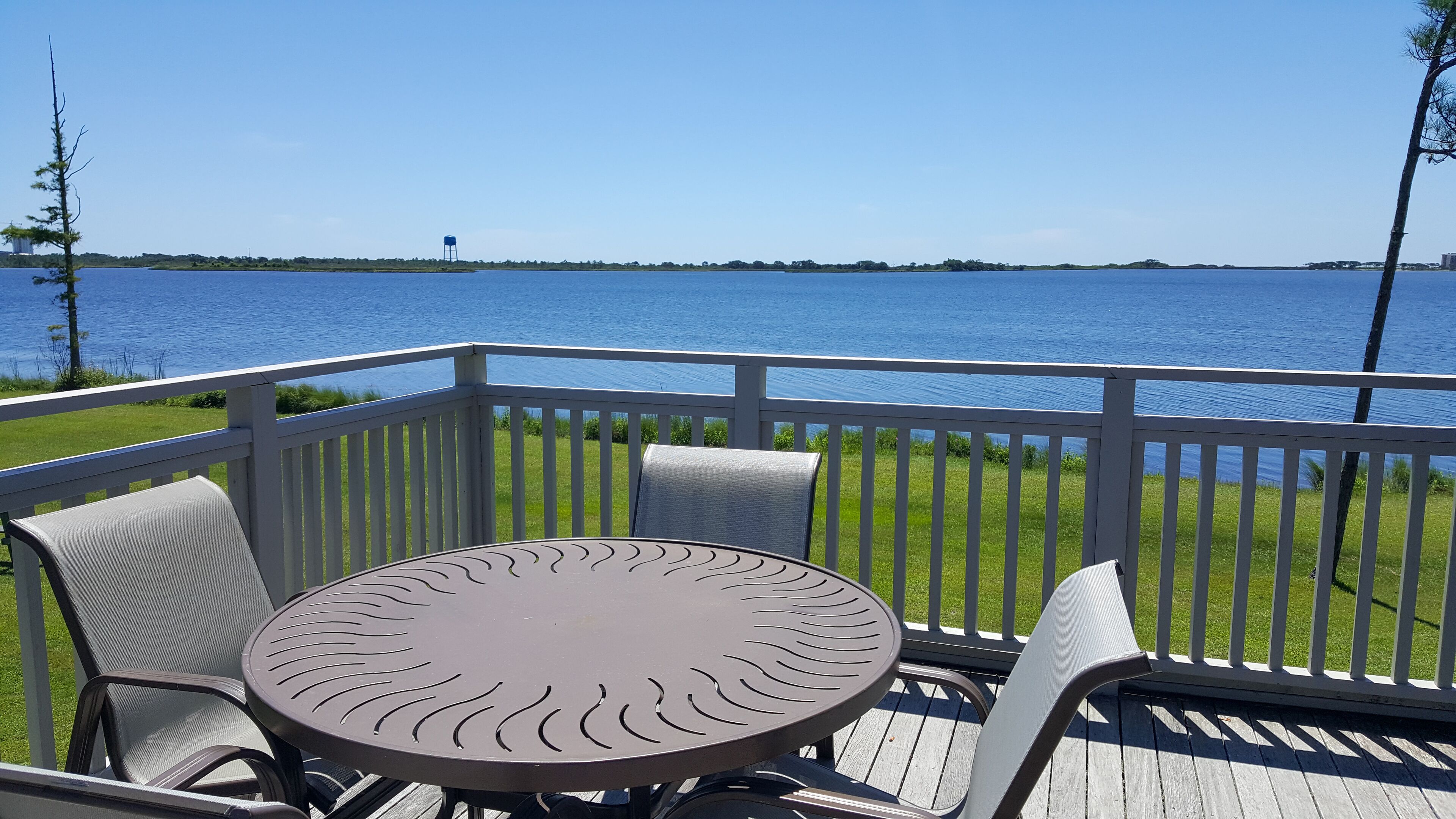 A deck with a round table and chairs, overlooking a body of water.