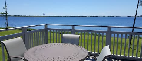 A deck with a round table and chairs, overlooking a body of water.