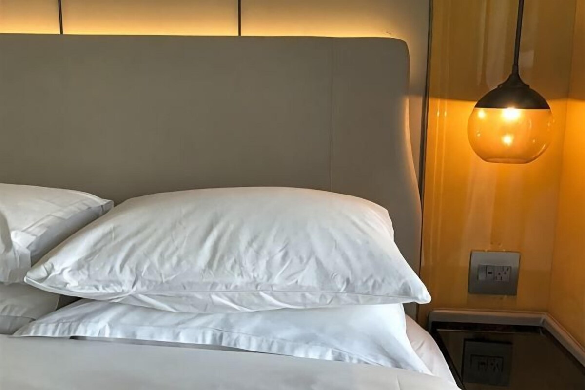 Un lit avec du linge de lit blanc et un luminaire fixé au mur.