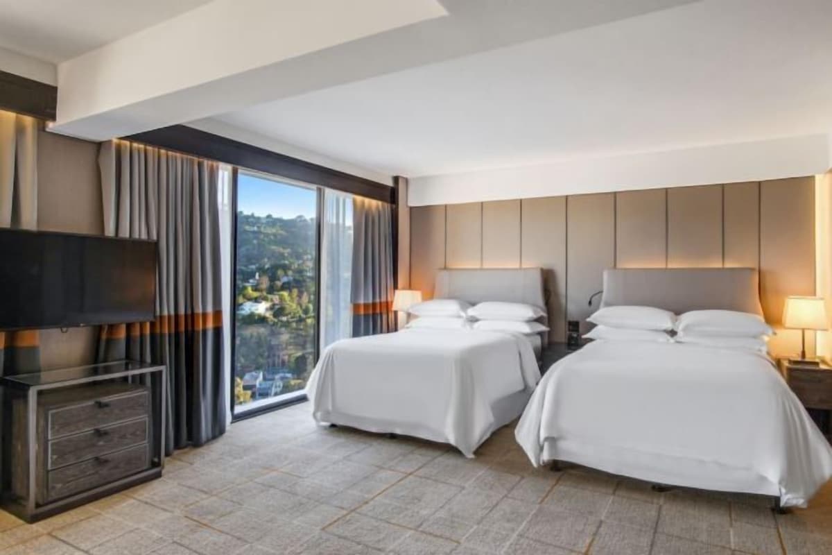 A hotel room with two beds, a TV, and a view of a mountainous landscape.