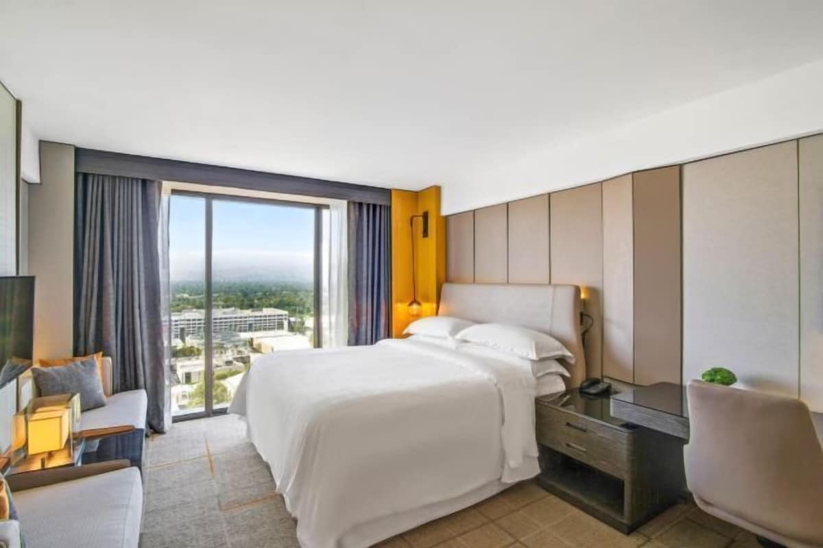 A hotel room with a large bed, a desk, a chair, and a view of the city.