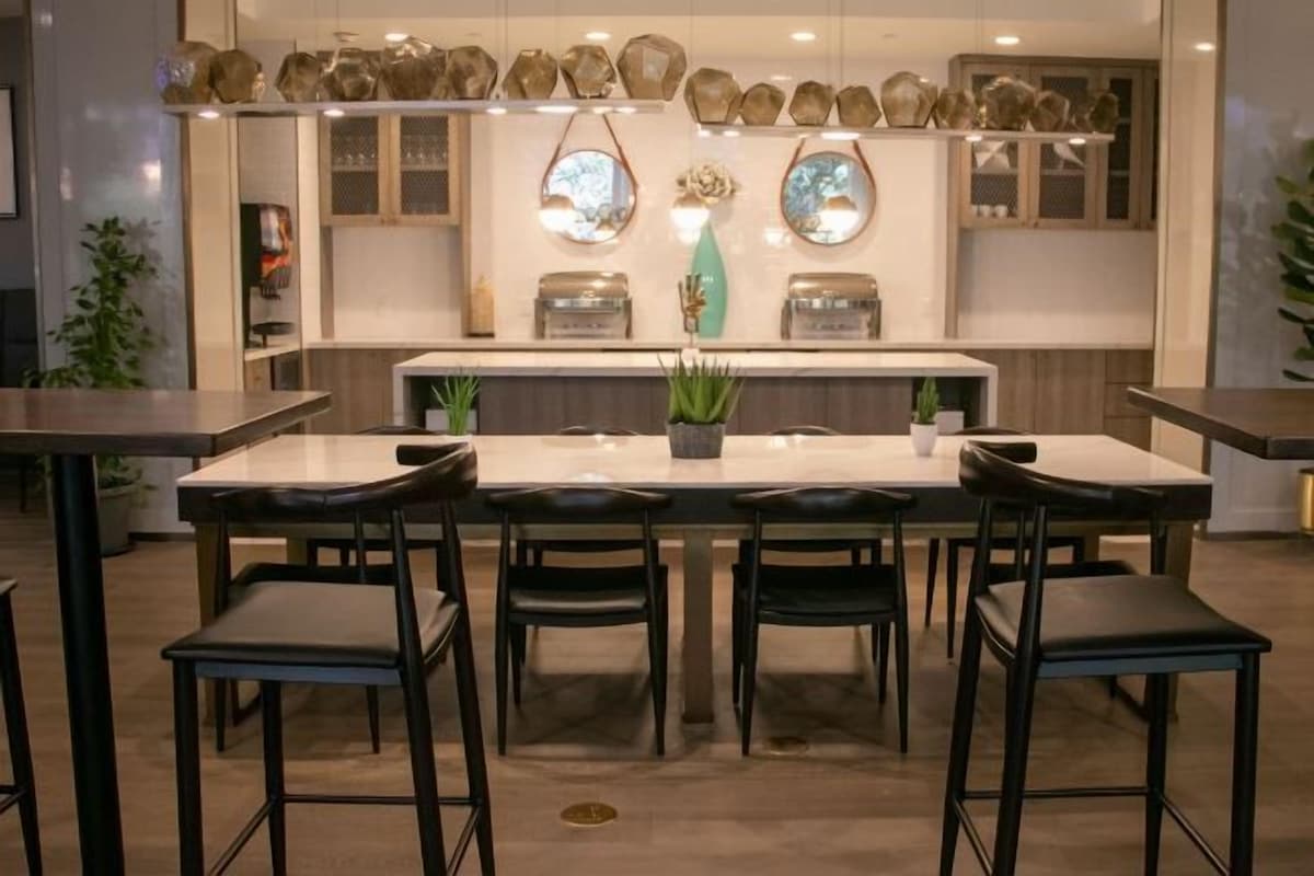 A modern bar area with a central island, black chairs, and decorative vases on shelves.