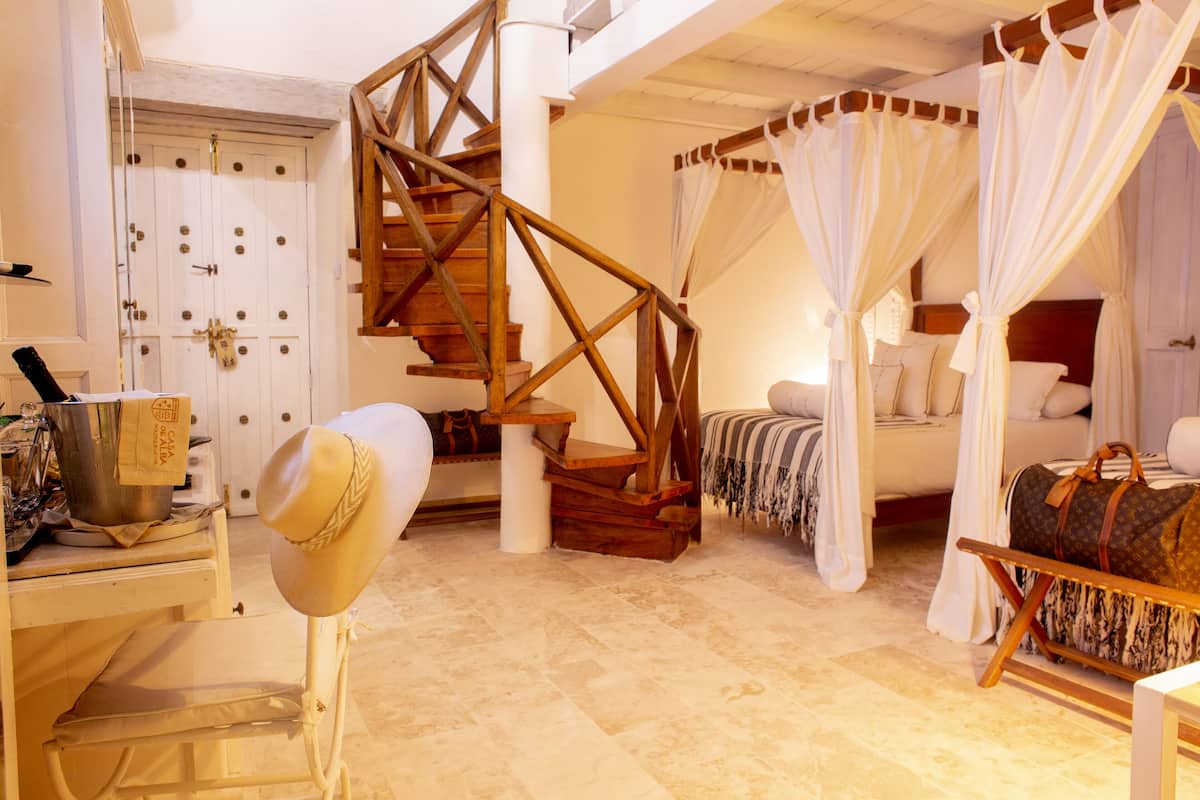 A bedroom with a wooden staircase, a bed with white curtains, and a suitcase on the floor.