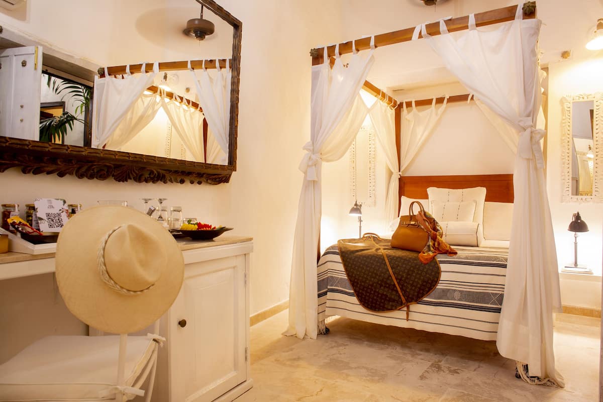 A bedroom with a canopy bed, a bedside table with a lamp, and a mirror above the bed.