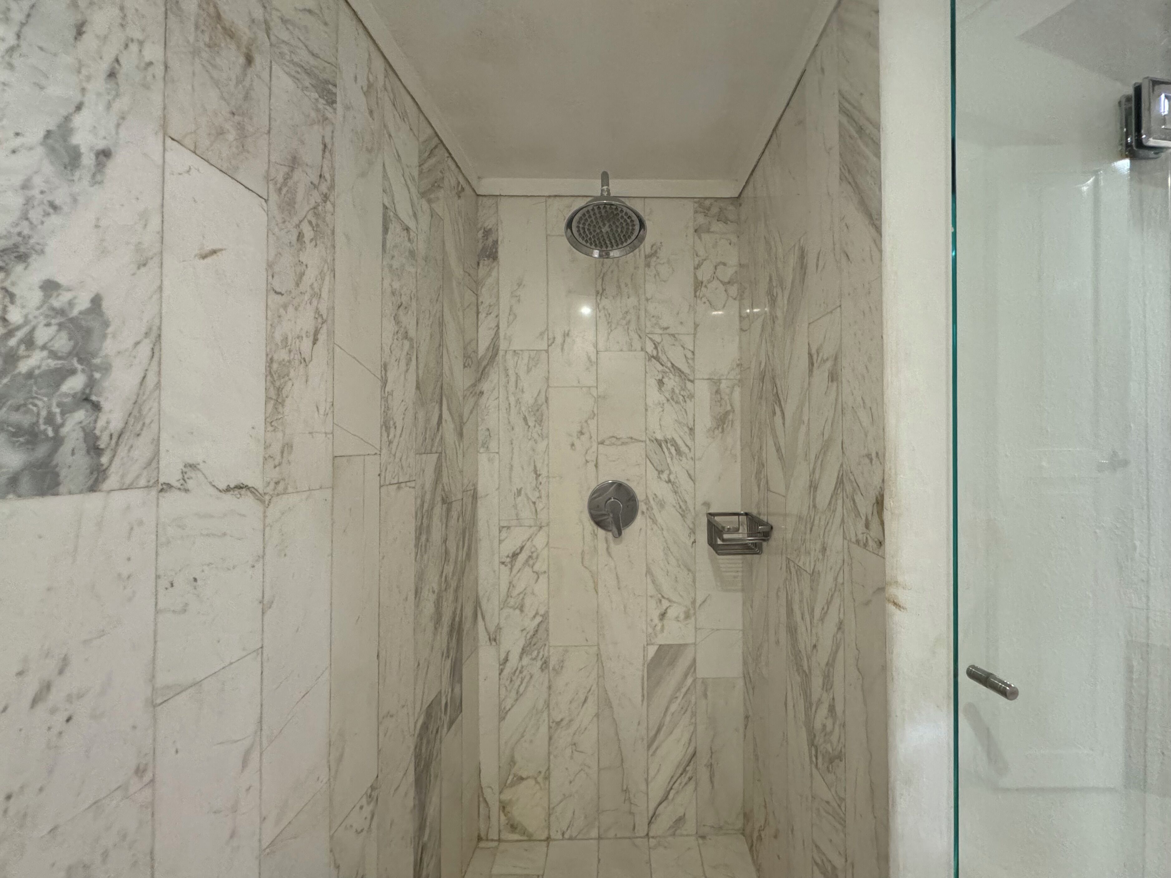 Une salle de bain aux murs recouverts de marbre et dotée d’une douche à parois de verre.