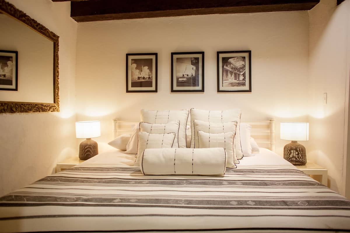 A neatly made bed with striped bedding, two bedside lamps, and three framed pictures on the wall.
