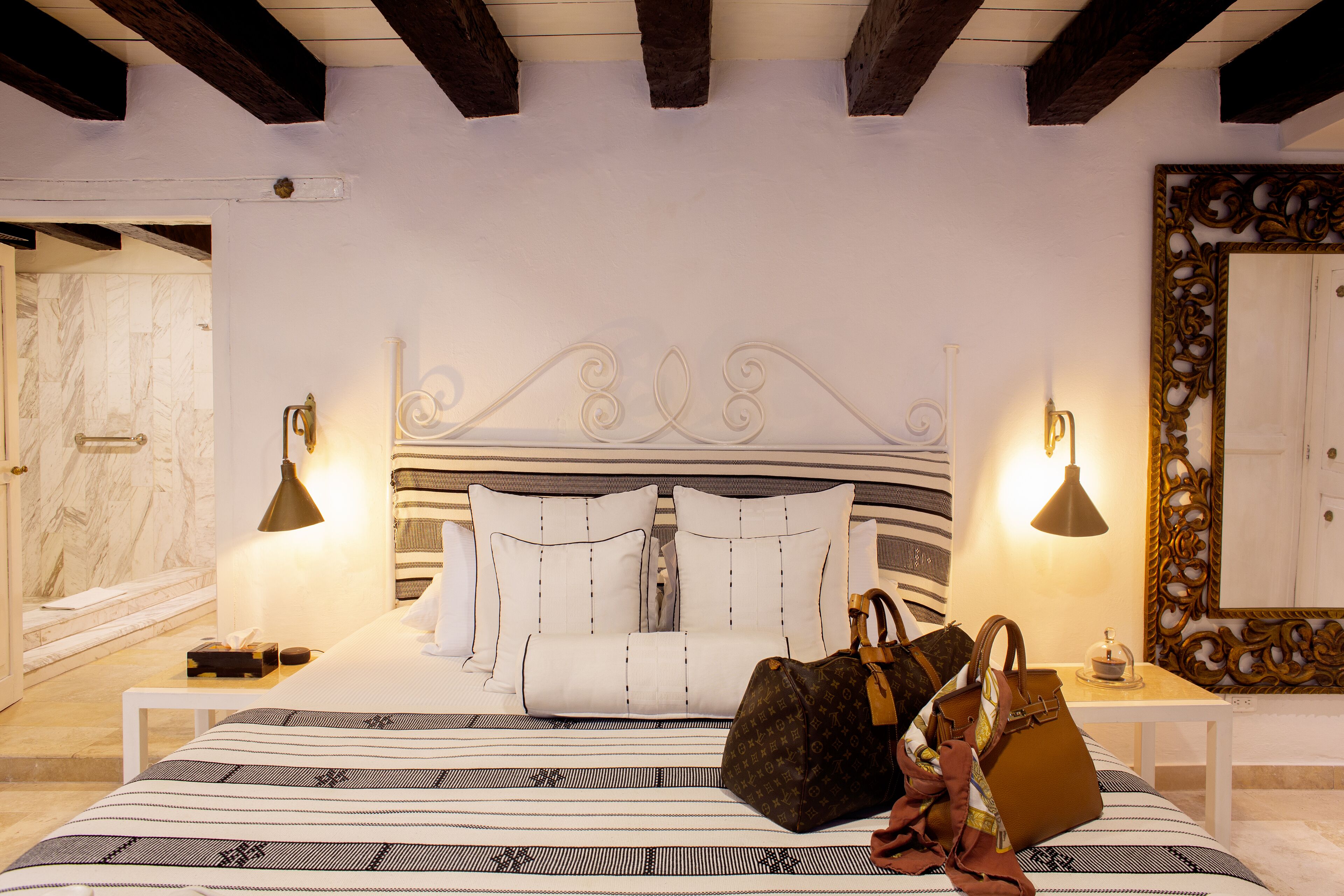 A bedroom with a large bed, a marble wall, a wooden ceiling, and a decorative mirror.