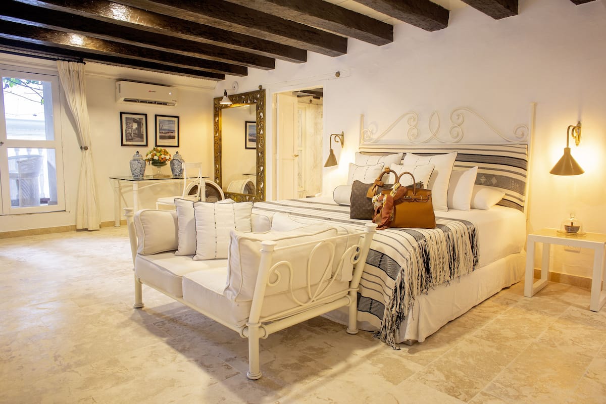 A bedroom with a bed, a sofa, a mirror, and a bedside table.