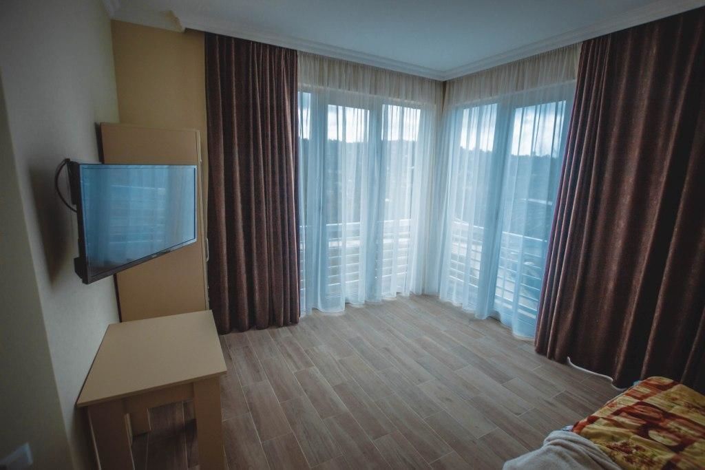 A hotel room with a television mounted on the wall, a small table, and a bed with a patterned bedspread.