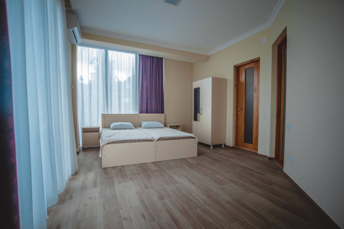 A bedroom with a bed, a wardrobe, a nightstand, and a window with curtains.