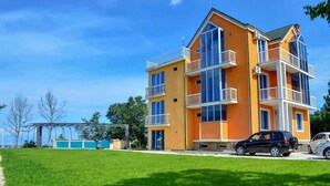 A multi-story residential building with balconies, a well-maintained lawn, and parked cars. - Private Villa Guest House (Khelvachauri)