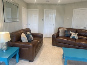 A living room with two brown leather sofas, a teal side table, and a mirror on the wall.