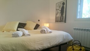 Una cama bien tendida con toallas enrolladas, un bolso amarillo y un par de botas en el suelo.