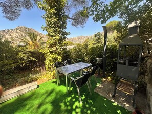 A patio with a table and chairs, surrounded by greenery and a view of hills.