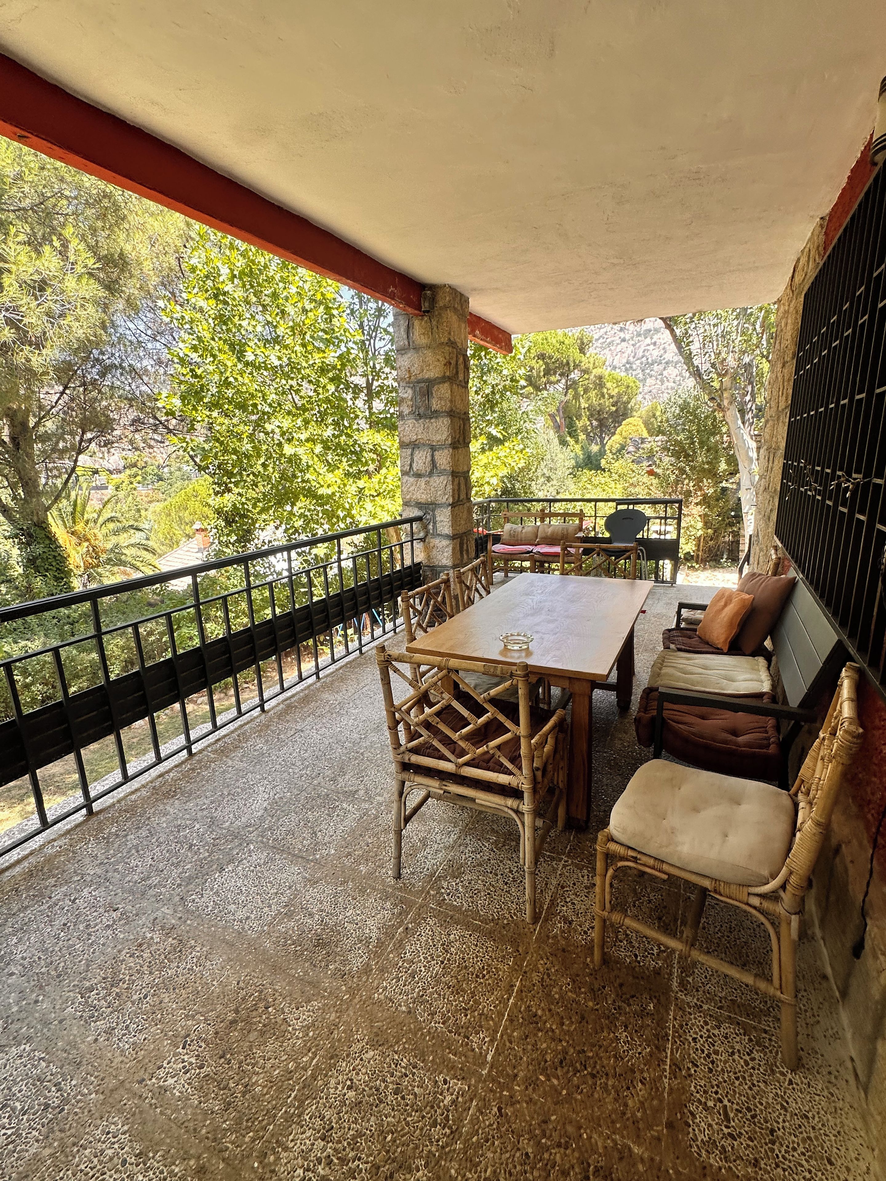 An outdoor patio with a table and chairs, surrounded by a stone floor and a black metal railing.