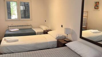 A hotel room with two beds, a radiator, a window with shutters, a bedside table with a lamp, and a mirror.