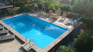 Una piscina rectangular con borde de hormigón, rodeada por una zona de terraza con sillas de descanso y un columpio.