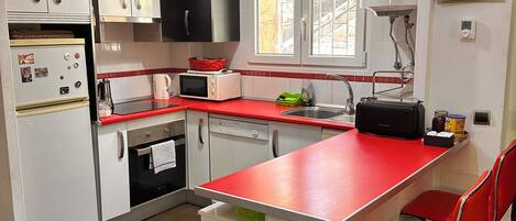 Una cucina con mobili bianchi, un piano di lavoro rosso, una sveglia e uno scaldabagno.