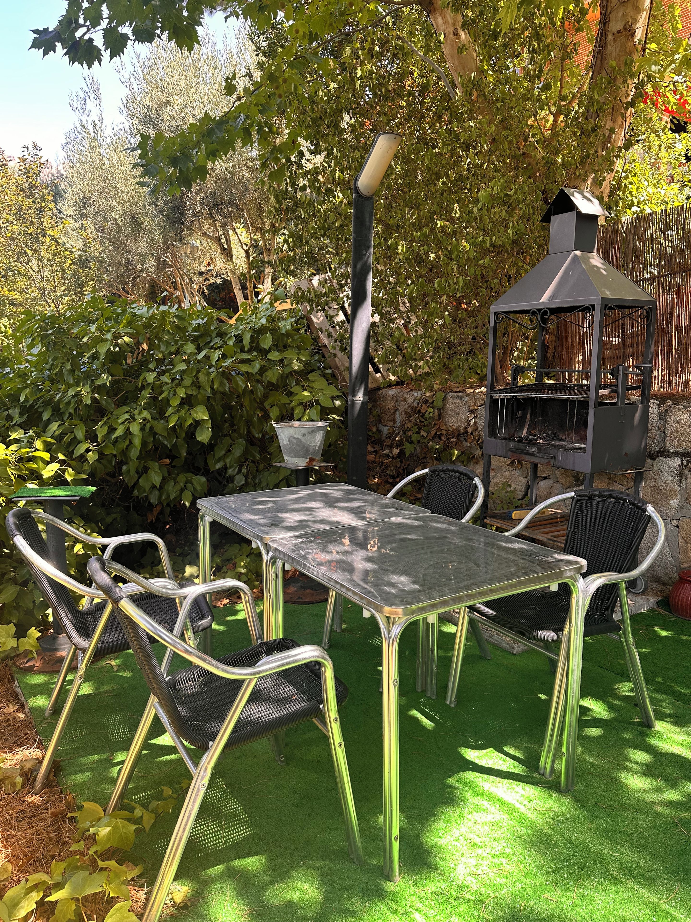 An outdoor patio with a table and chairs, a grill, and a tree providing shade.