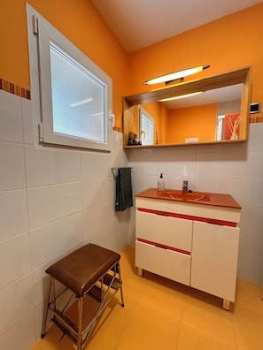 Un baño con tocador blanco, espejo, ventana y banco.