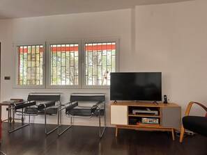 Una sala de estar con televisor, dos sillones, un mueble con reproductor de DVD y una ventana con rejas.