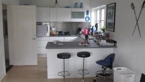 A compact kitchen with a central island, two bar stools, a small bar chair, and a sink. - Guesthouse Sharon Suite (Aarhus)