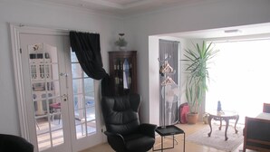 A living room with a black leather chair, a small table, a red patterned rug, and a potted plant. - Guesthouse Sharon Suite (Aarhus)