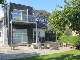 Et moderne hus med to etager, en altan, en terrasse med udendørs møbler og en grill.