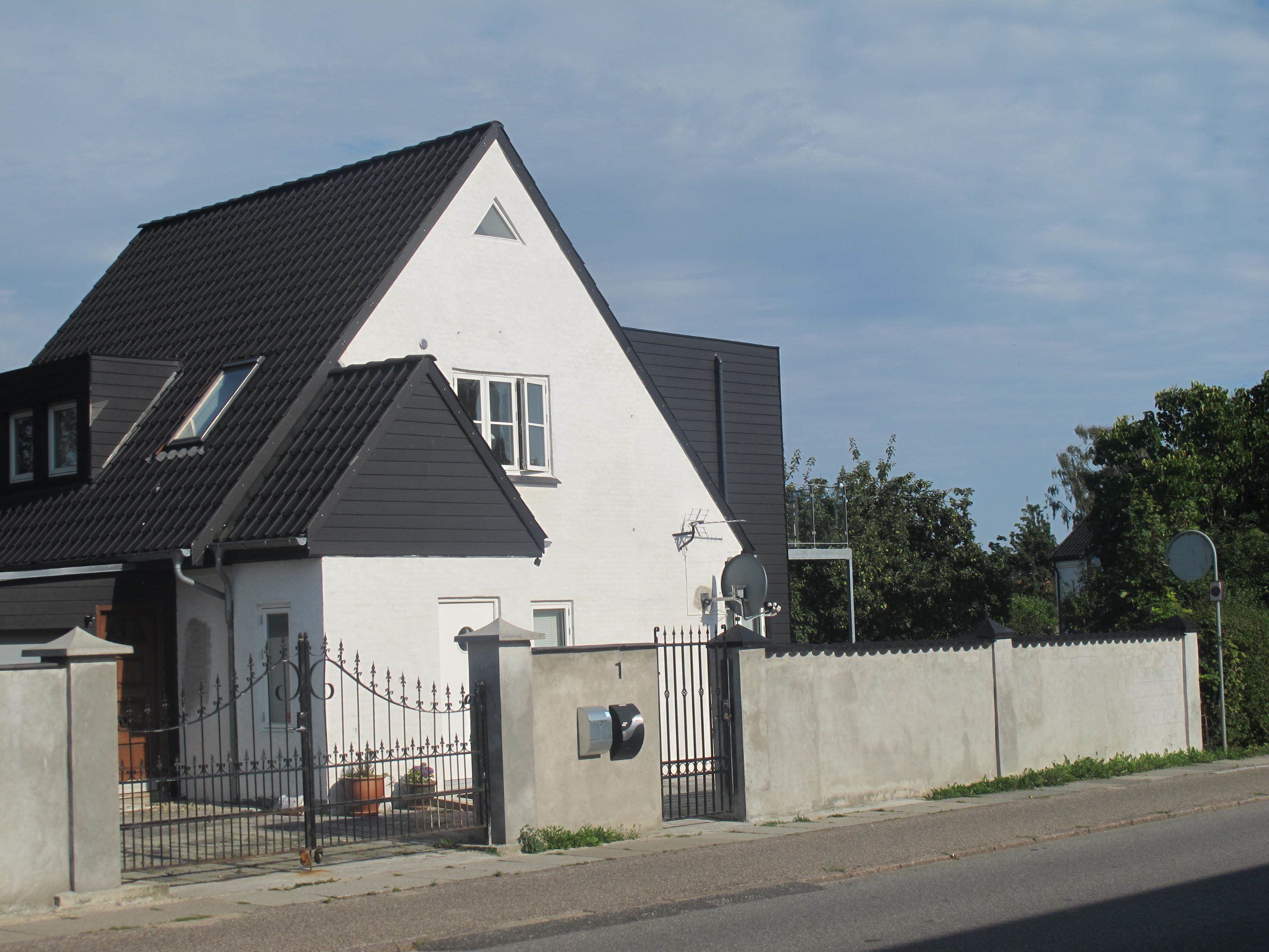 A white house with a dark roof, a gated entrance, and a mailbox.