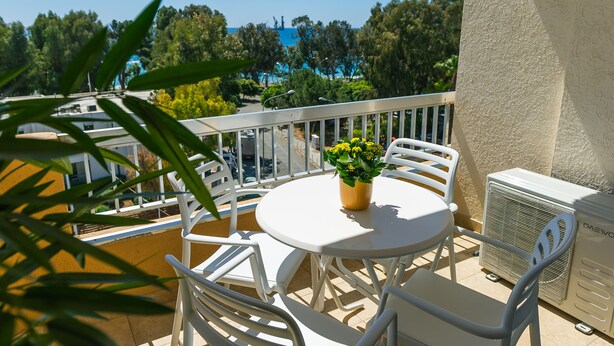 A balcony with a round table and chairs, a potted plant, and an air conditioning unit. - Pebble Beach Holiday Apartments (Limassol)