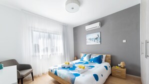 A modern bedroom with a bed, bedside tables, a chair, and a desk. - Pebble Beach Holiday Apartments (Limassol)