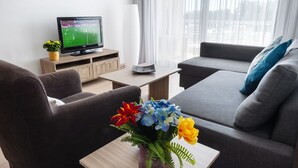 A modern living room with a flat-screen TV, a sofa, a coffee table, and a vase with flowers. - Pebble Beach Holiday Apartments (Limassol)
